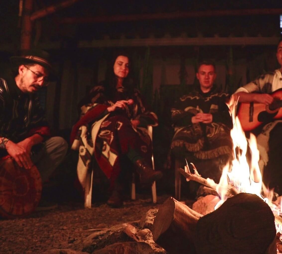 Eine Menschen sitzen während der Ayahuasca Zeremonie gemeinsam am Feuer und musizieren zusammen